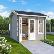 A light gray wooden garden shed with white doors and a black roof, shown in a landscaped backyard with a green lawn, flowers, trees, and a blue sky.